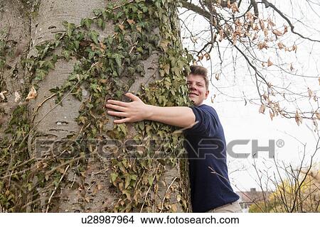 Picture - Teenage boy hugging wide tree trunk in garden. Fotosearch