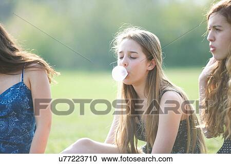 Stock Image - Teenage girl blowing bubble gum bubble in park. Fotosearch