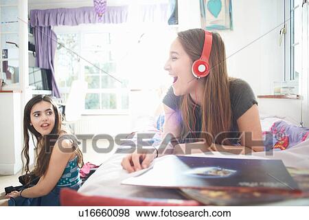 Teenage girl chatting to friend whilst listening to headphones in bedroom View Large Photo Image Stock Photo - Teenage girl chatting to friend whilst listening to headphones in bedroom. Fotosearch