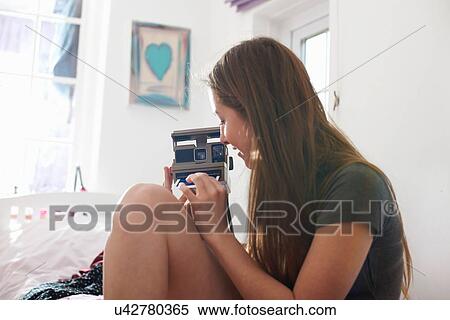 Teenage girl in bedroom removing instant photograph from camera View Large Photo Image Stock Photography - Teenage girl in bedroom removing instant photograph from camera. Fotosearch
