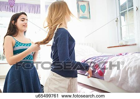 Stock Image - Teenage girl plaiting best friends hair in bedroom. Fotosearch