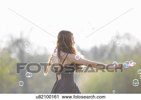 Teenage girl spinning bubbles with bubble wand in park View Large Photo Image Stock Image - Teenage girl spinning bubbles with bubble wand in park. Fotosearch