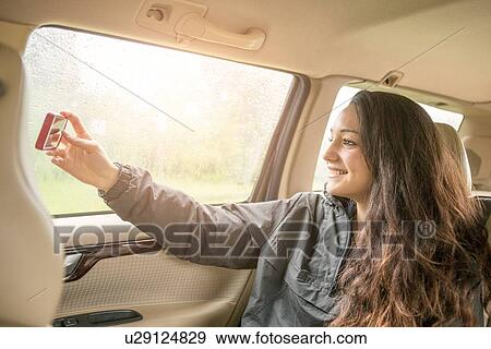 Stock Photo - Teenage girl taking smartphone selfie in car back seat. Fotosearch