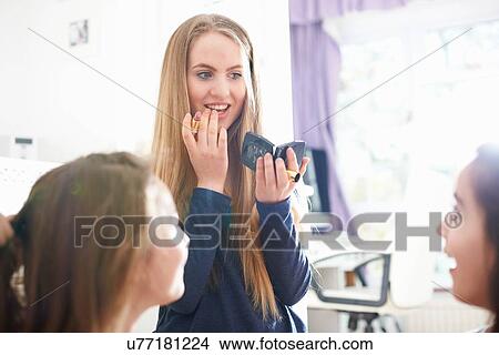 Picture - Teenage girl with friends applying lipstick in bedroom. Fotosearch
