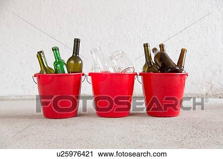 Stock Image - Three recycling buckets in garage with green, brown and transparent bottles. Fotosearch
