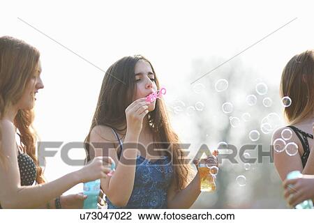 Three teenage girls blowing bubbles in park View Large Photo Image Stock Image - Three teenage girls blowing bubbles in park. Fotosearch