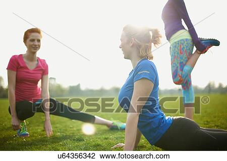 Stock Image - Three women exercising and stretching in the park. Fotosearch