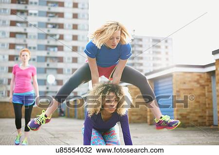 Stock Image - Three women exercising together wearing sports clothing and playing leap frog. Fotosearch