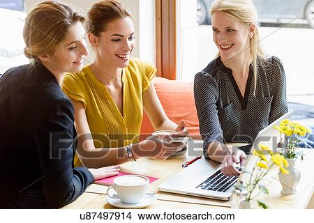Picture - Three young women looking at laptop in cafe. Fotosearch