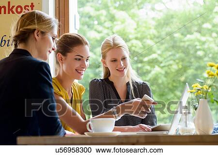 Stock Image - Three young women pointing at laptop in cafe. Fotosearch