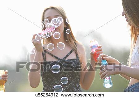 Stock Image - Two teenage girls blowing bubbles in park. Fotosearch
