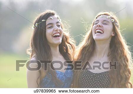 Stock Photography - Two teenage girls wearing daisy chain headdresses laughing in park. Fotosearch