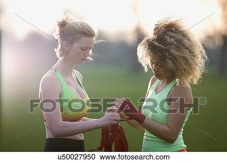 Stock Image - Two women applying hand straps for boxing gloves in the park. Fotosearch