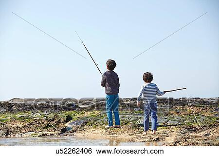 Stock Photograph - Two young boys, fishing on beach, rear view. Fotosearch