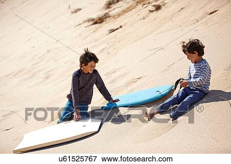 Stock Photo - Two young boys sitting on sandy hill with sledges beside them. Fotosearch