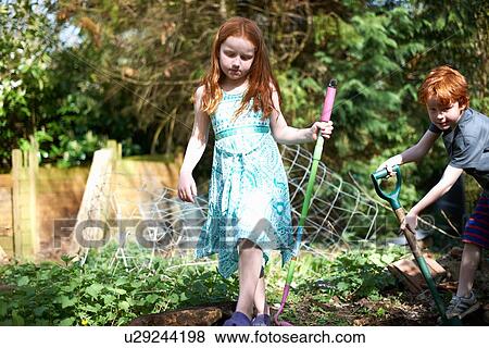 Stock Photo - Two young children in garden, holding gardening tools. Fotosearch