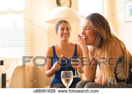 Stock Photo - Two young woman having girls night in, drinking and laughing. Fotosearch
