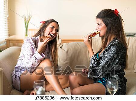 Two young women having girls night in, sitting on sofa, eating and laughing View Large Photo Image Stock Image - Two young women having girls night in, sitting on sofa, eating and laughing. Fotosearch
