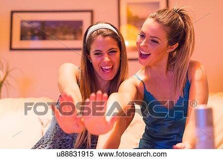 Stock Photography - Two young women having girls night in, looking at newly painted nails. Fotosearch