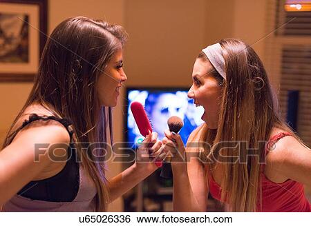 Stock Photograph - Two young women, singing into hair and make-up brushes. Fotosearch