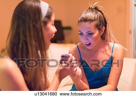 Two young women sitting on sofa, looking at smartphones, laughing View Large Photo Image Stock Image - Two young women sitting on sofa, looking at smartphones, laughing. Fotosearch
