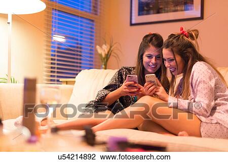 Two young women sitting on sofa, looking at smartphones, laughing View Large Photo Image Stock Image - Two young women sitting on sofa, looking at smartphones, laughing. Fotosearch