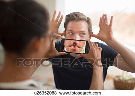 Stock Photo - Woman holding smartphone in front of man's mouth. Fotosearch