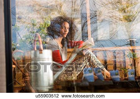 Stock Image - Woman reading a book, view through window. Fotosearch