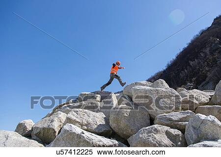 Stock Photography - Worker jumping on stack of boulders at quarry. Fotosearch
