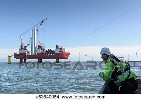Picture - Worker looking at construction ship and offshore windfarm. Fotosearch