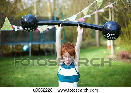 Stock Image - Young boy lifting pretend barbell, outdoors. Fotosearch