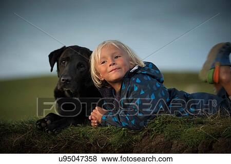 Stock Photo - Young boy lying down with dog in field. Fotosearch