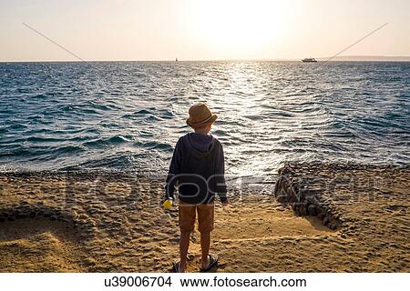 Picture - Young boy standing by sea, looking at view, rear view, Hurgada, Red Sea, Egypt. Fotosearch