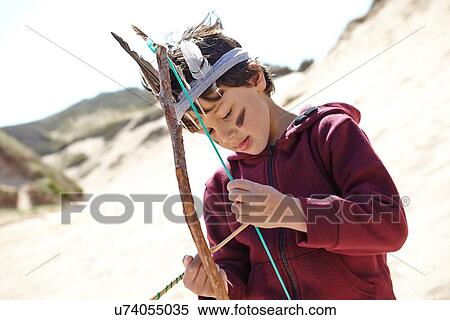 Stock Photography - Young boy wearing fancy dress, holding home-made bow and arrow. Fotosearch