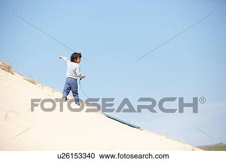 Stock Image - Young boy with sledge on sandy hill. Fotosearch