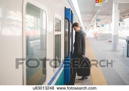 Stock Photo - Young businessman commuter boarding train with suitcase.. Fotosearch
