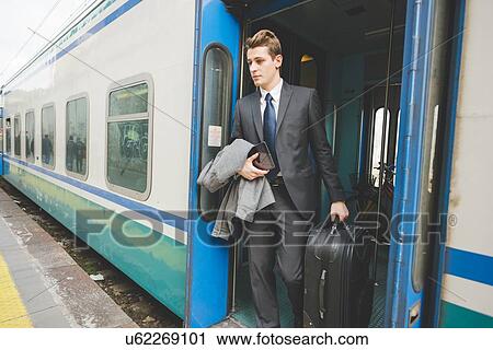 Stock Image - Young businessman commuter exiting train with suitcase.. Fotosearch