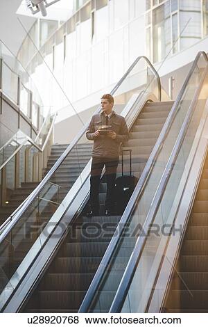 Stock Photo - Young businessman commuter on escalator with suitcase.. Fotosearch