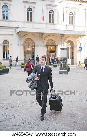 Young businessman commuter walking along cobbled street with suitcase. View Large Photo Image Stock Photo - Young businessman commuter walking along cobbled street with suitcase.. Fotosearch