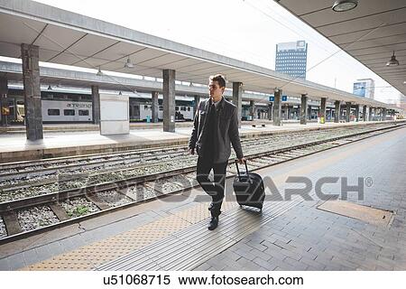 Young businessman commuter walking along train station platform pulling suitcase. View Large Photo Image Stock Photography - Young businessman commuter walking along train station platform pulling suitcase.. Fotosearch