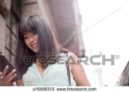 Stock Image - Young businesswoman, using smartphone, outdoors, Shanghai, China. Fotosearch