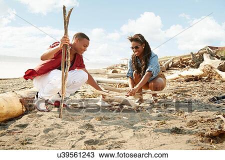 Young couple crouching on beach building campfire with drftwood View Large Photo Image Stock Image - Young couple crouching on beach building campfire with drftwood. Fotosearch