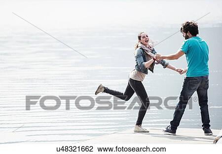 Stock Image - Young couple fooling around on pier at Lake Mergozzo, Verbania, Piemonte, Italy. Fotosearch