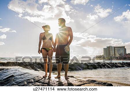 Young couple holding hands on rocks at Waikiki Beach, Hawaii, USA View Large Photo Image Picture - Young couple holding hands on rocks at Waikiki Beach, Hawaii, USA. Fotosearch