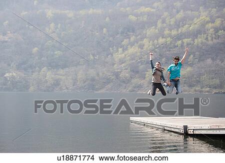 Young couple jumping mid air on pier at Lake Mergozzo, Verbania, Piemonte, Italy View Large Photo Image Picture - Young couple jumping mid air on pier at Lake Mergozzo, Verbania, Piemonte, Italy. Fotosearch