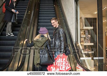 Young couple moving up escalator with shopping bags, New York, USA View Large Photo Image Stock Image - Young couple moving up escalator with shopping bags, New York, USA. Fotosearch