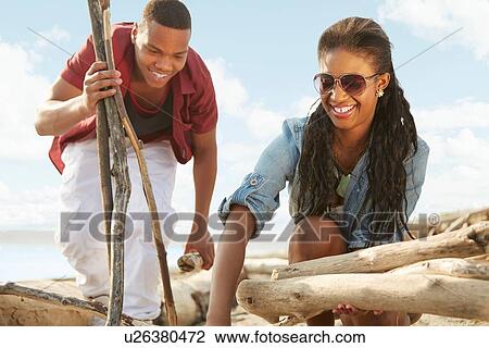 Stock Image - Young couple on beach gathering driftwood together. Fotosearch