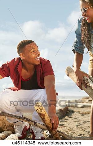 Young couple on beach gathering driftwood together, face to face View Large Photo Image Stock Photography - Young couple on beach gathering driftwood together, face to face. Fotosearch