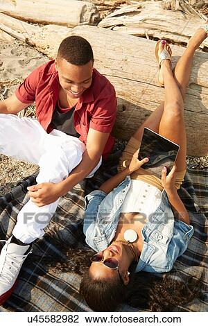 Stock Image - Young couple relaxing together on beach using digital tablet, overhead view. Fotosearch