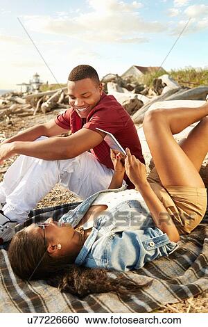 Young couple relaxing together on beach using digital tablet View Large Photo Image Stock Image - Young couple relaxing together on beach using digital tablet. Fotosearch